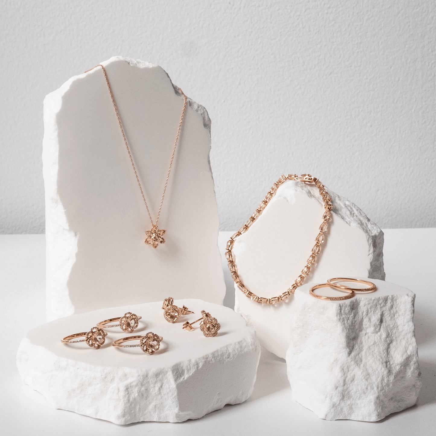 Rose gold jewelry set including necklace, bracelet, and rings displayed on white stone blocks.