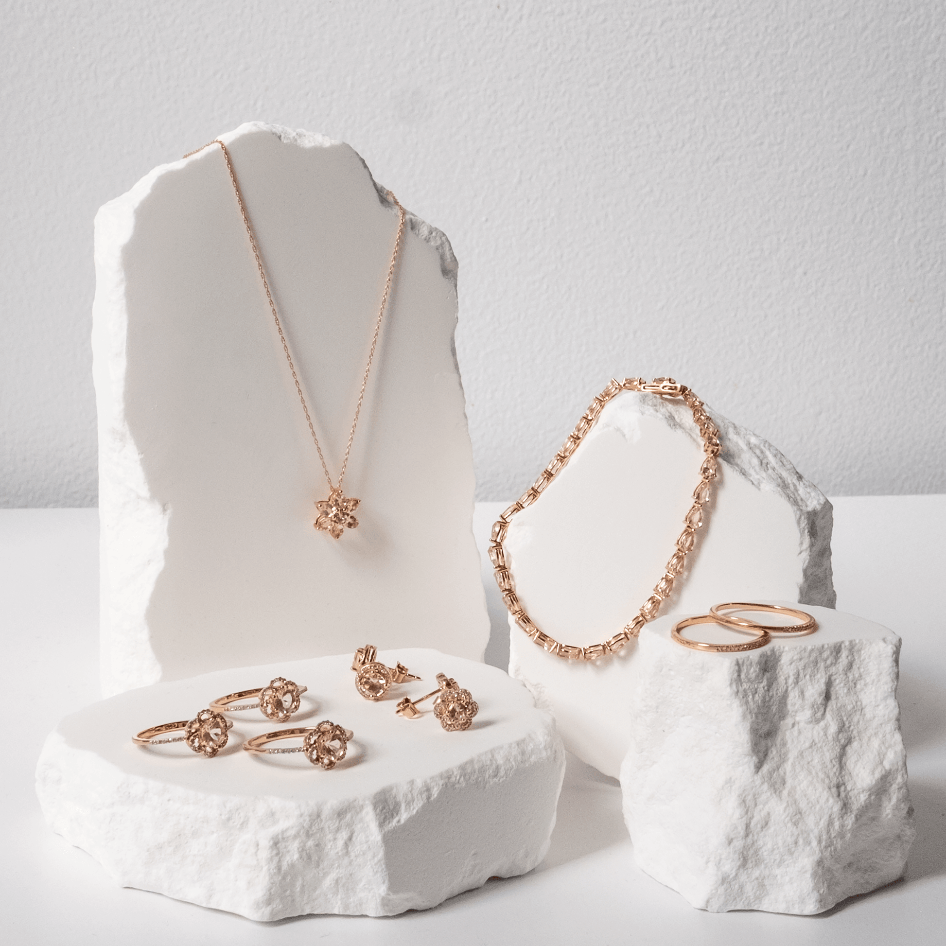 Rose gold jewelry set including necklace, bracelet, and rings displayed on white stone blocks.