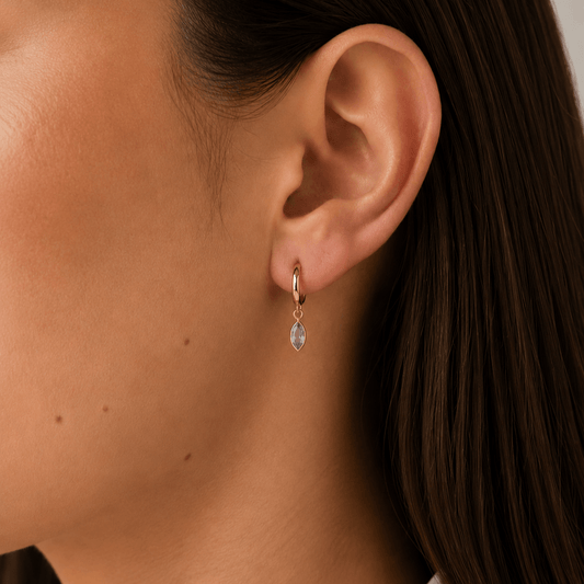 Close-up of an ear with a gold hoop earring and a teardrop-shaped earring.