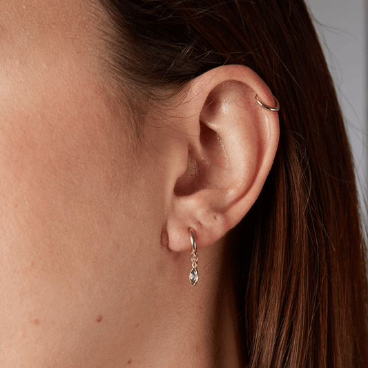 Close-up of an ear with a gold hoop earring and a teardrop-shaped earring.