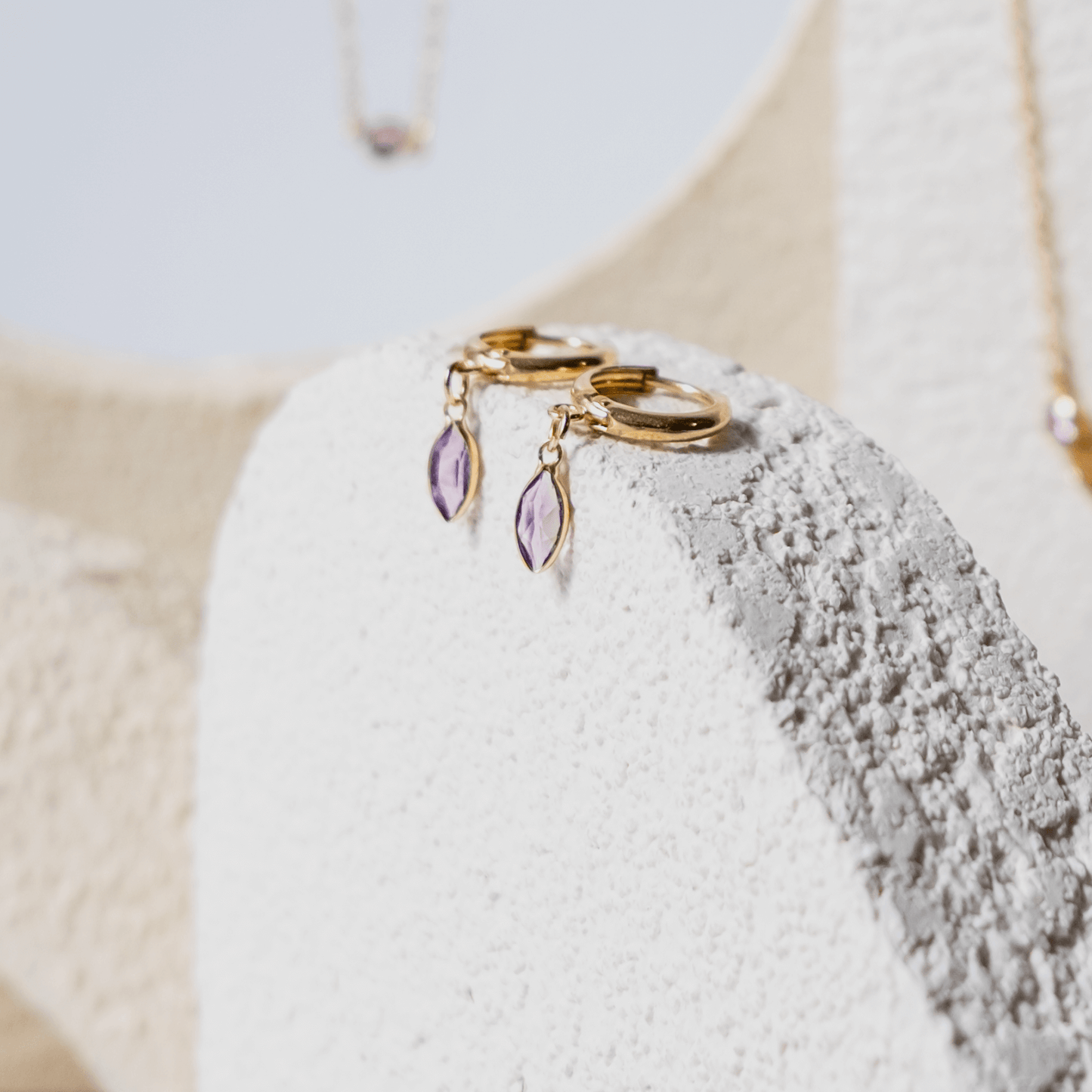 Gold earrings with purple stones on a textured white surface