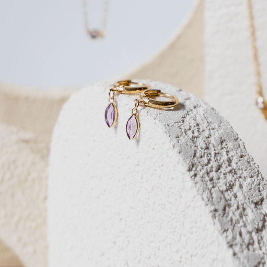 Gold earrings with purple stones on a textured white surface