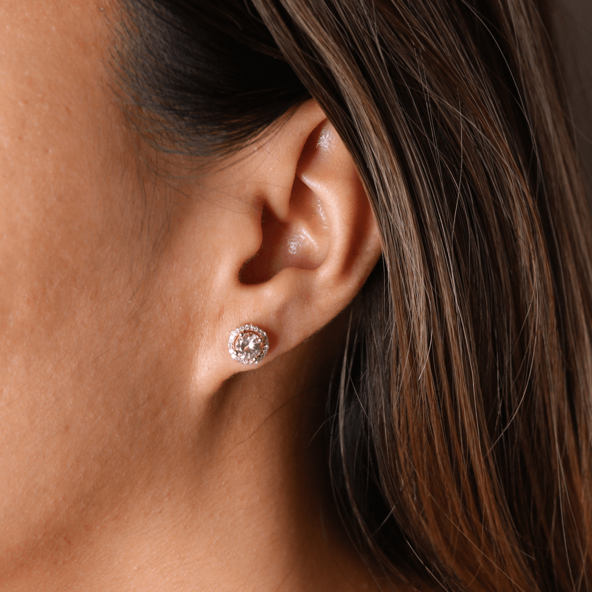 Close-up of an ear wearing a diamond earring with hair partially covering the face.