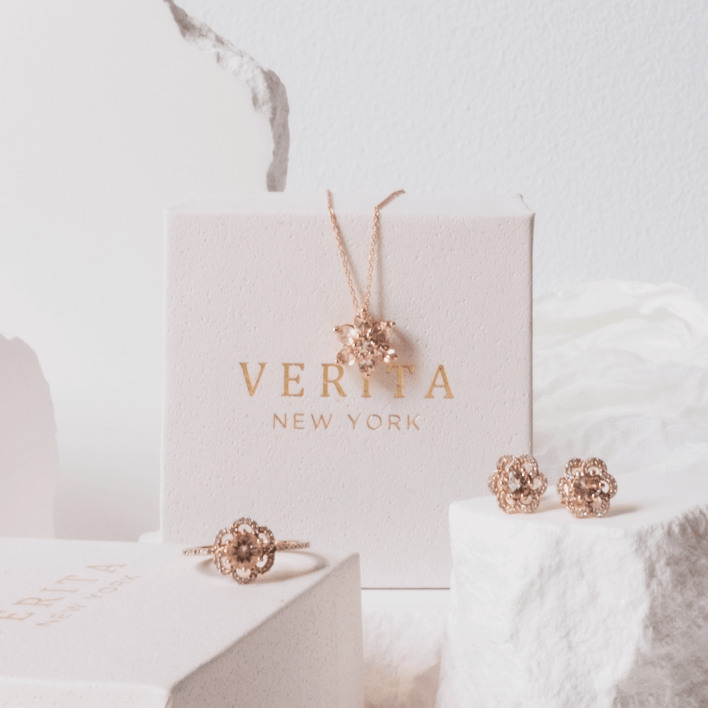 Rose gold jewelry set including earrings and a ring on a white surface with 'VERITA NEW YORK' branding.