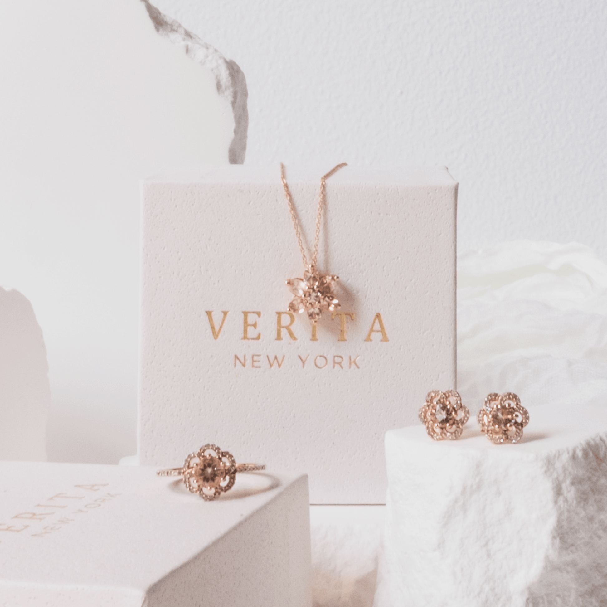 Rose gold jewelry set including earrings and a ring on a white surface with 'VERITA NEW YORK' branding.