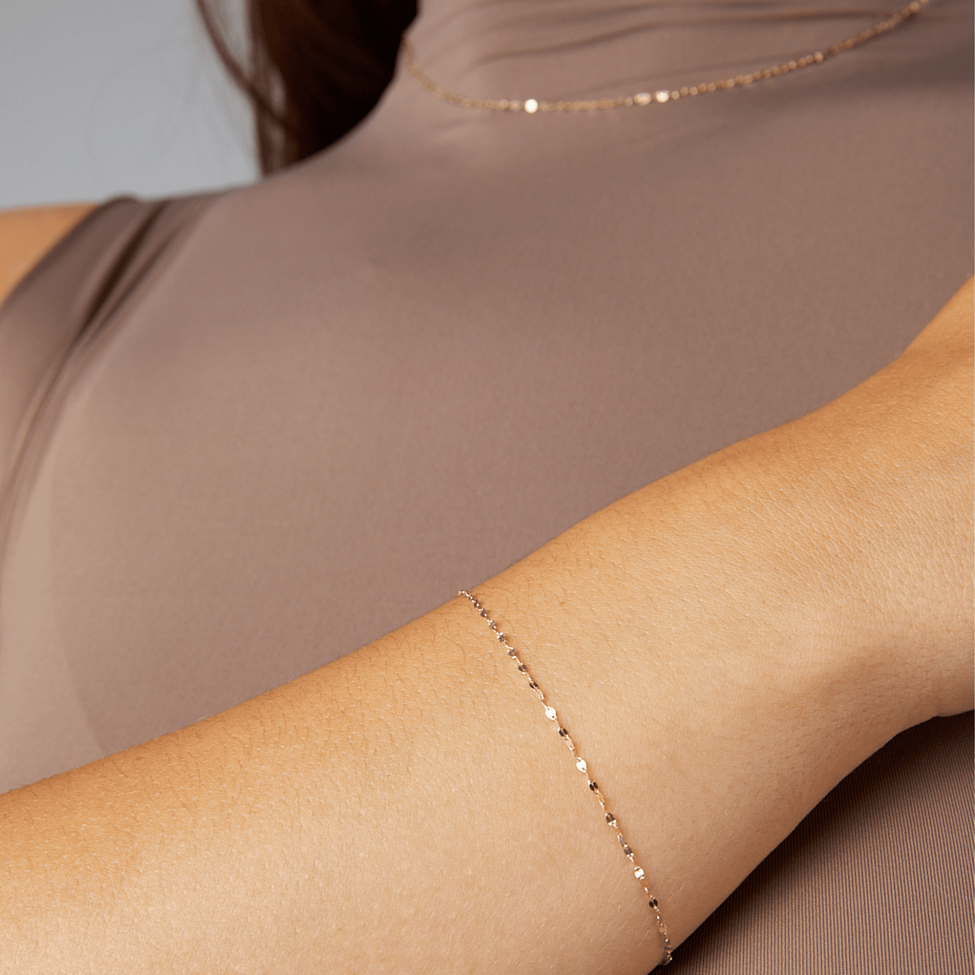 Close-up of a person wearing a delicate gold bracelet on a neutral background