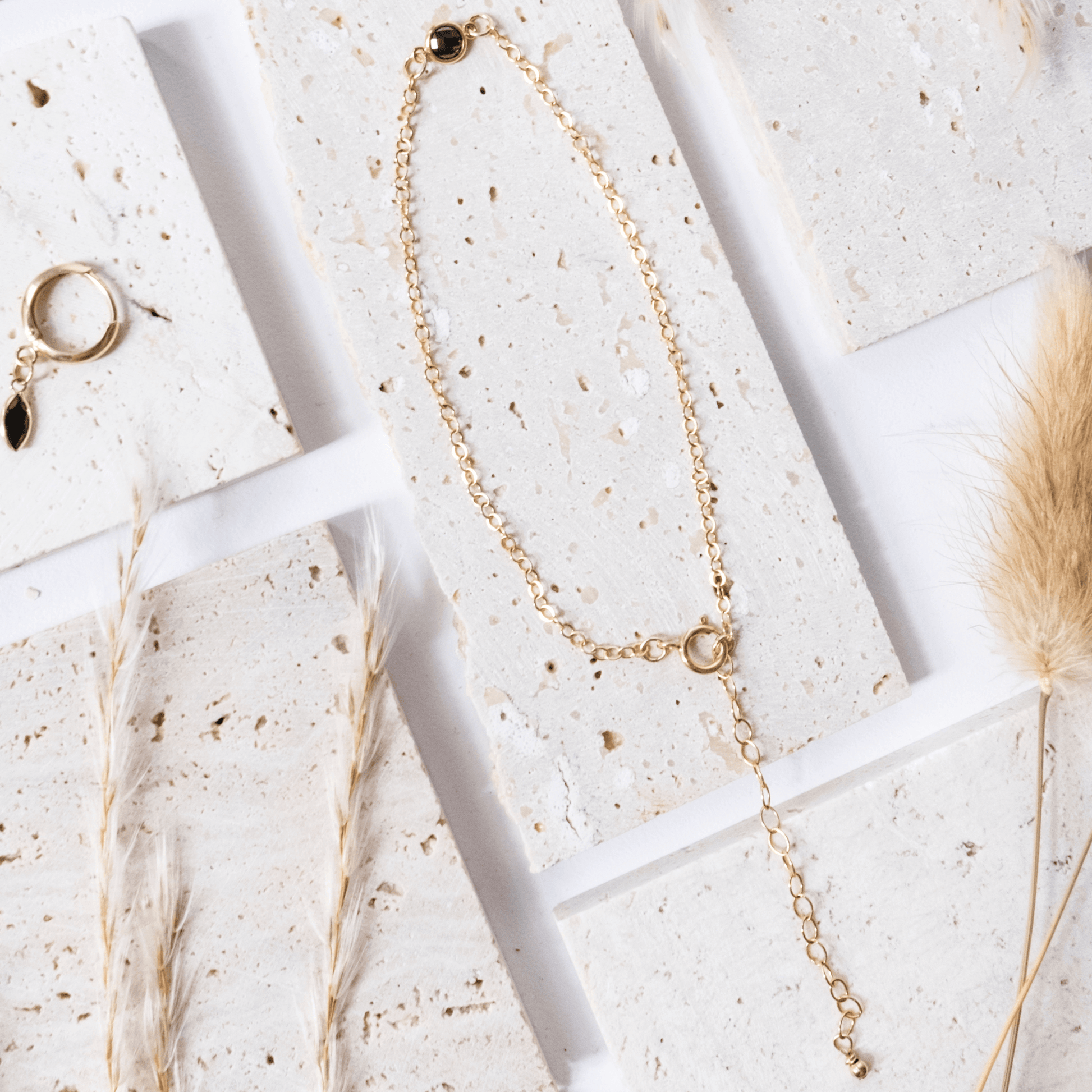 Gold necklace on a textured white surface with dried grasses