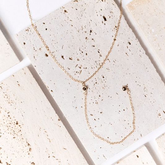 Gold necklace and earring set on a textured stone surface