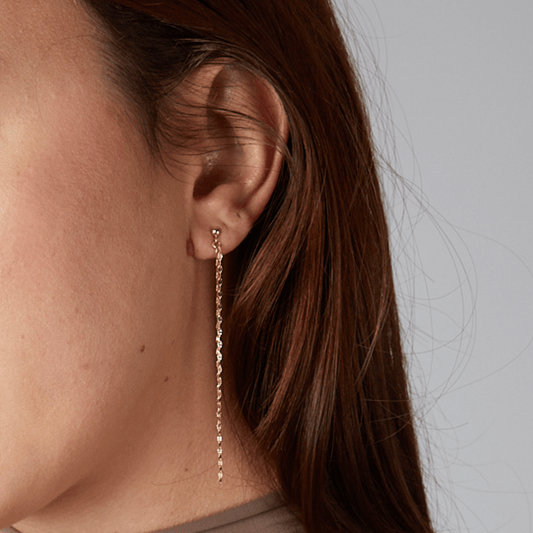 Close-up of an ear wearing a gold chain earring with a plain background