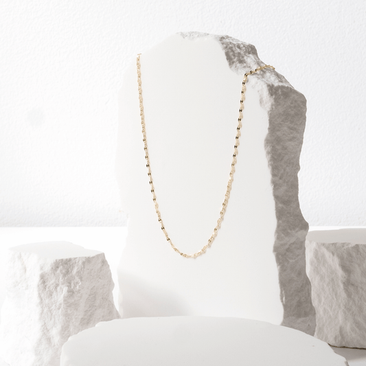 Gold necklace on a white and gray stone surface