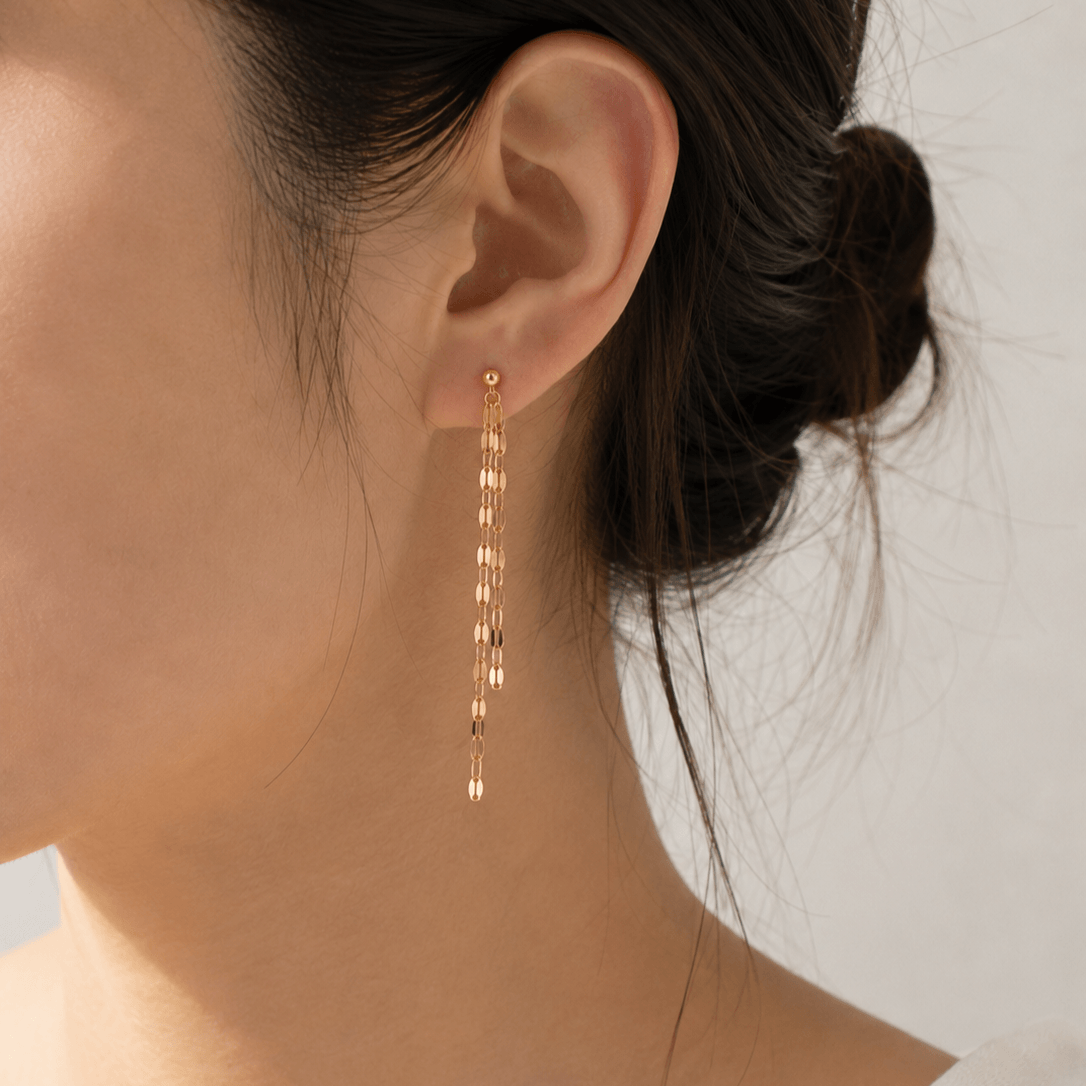 A close-up of a model's ear wearing a delicate gold dangle earring with multiple small linked drops.