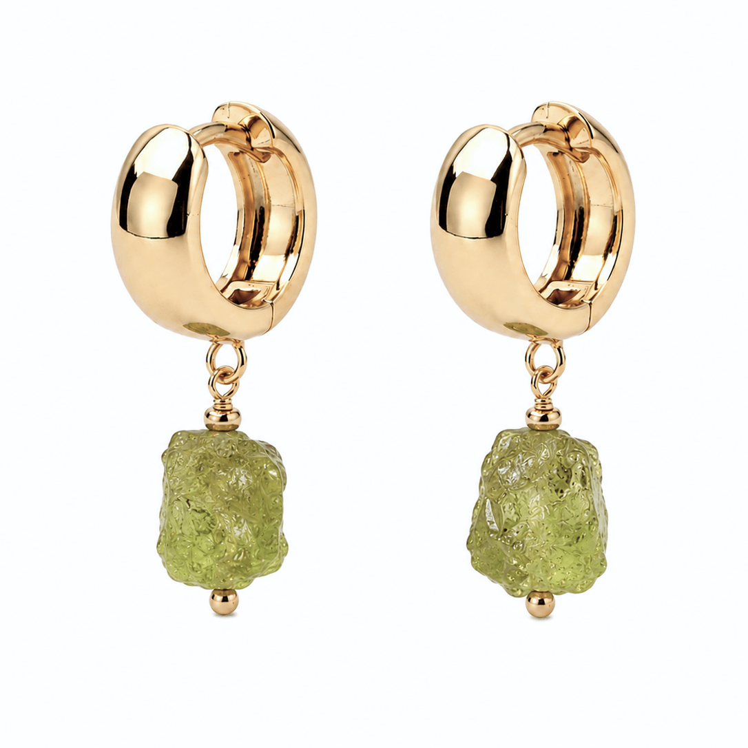 A pair of gold huggie hoop earrings with a dangling raw green gemstone, shown on a solid white background.