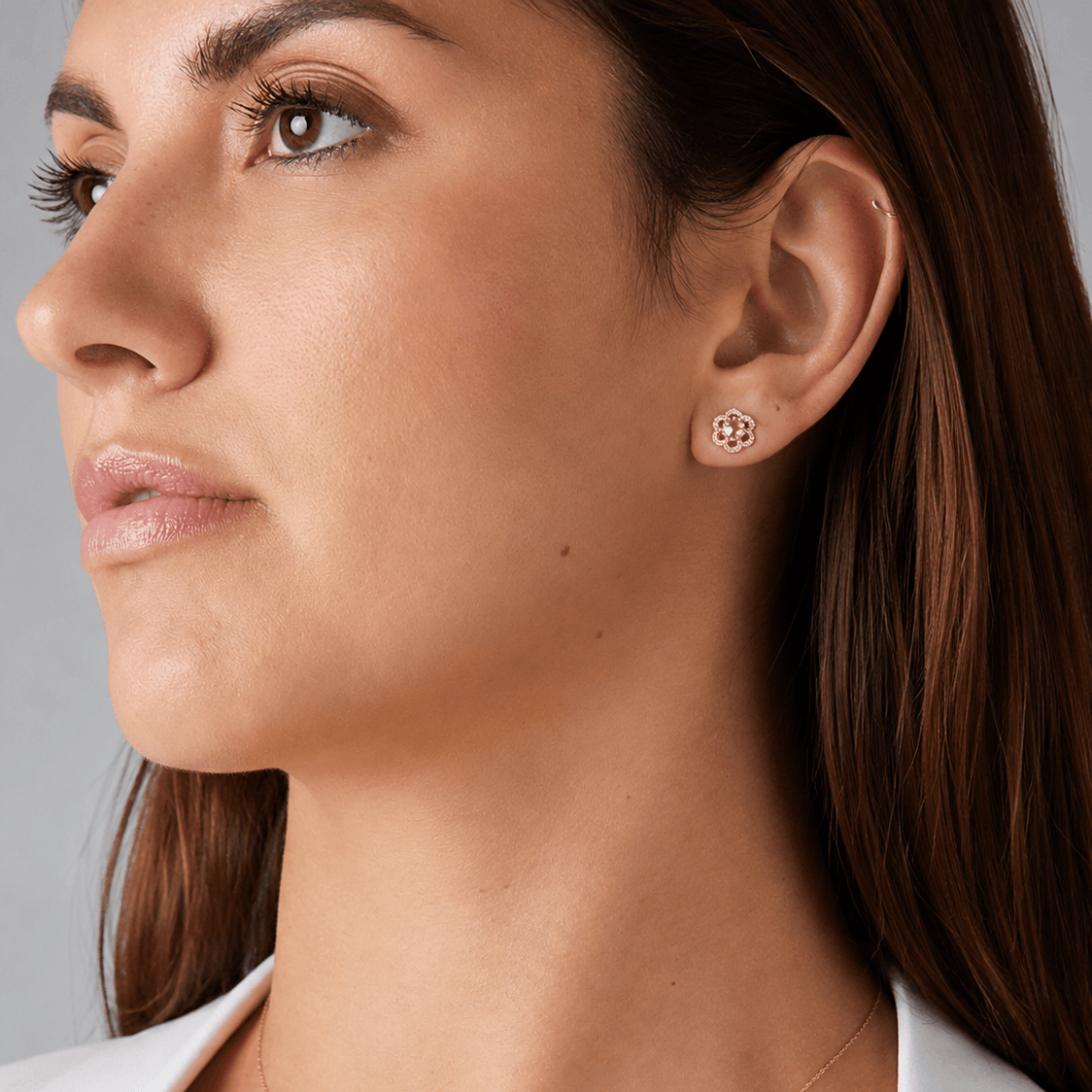 Close-up side profile of a woman wearing a small circular floral rose gold stud earring with a morganite gemstone center, set against a neutral gray background.