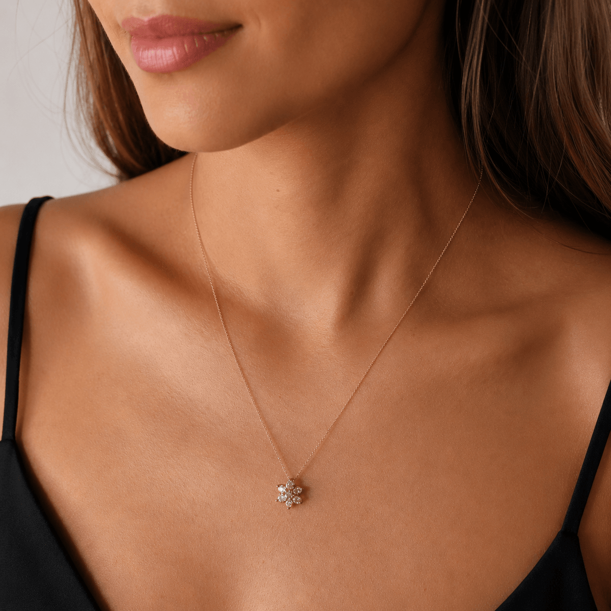 A close-up of a woman wearing a delicate rose gold chain necklace with a small flower-shaped cluster pendant set with morganite and diamonds.